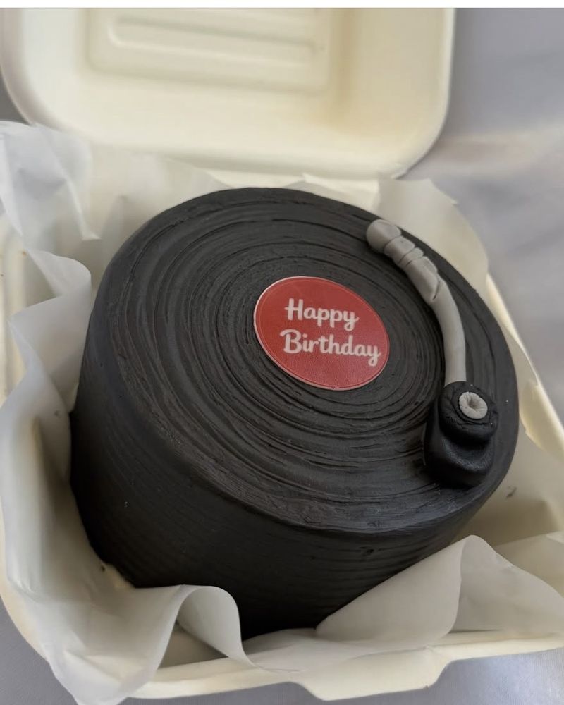 Bento cake noir en forme de disque vinyle avec étiquette rouge « Happy Birthday », présenté dans sa boîte
