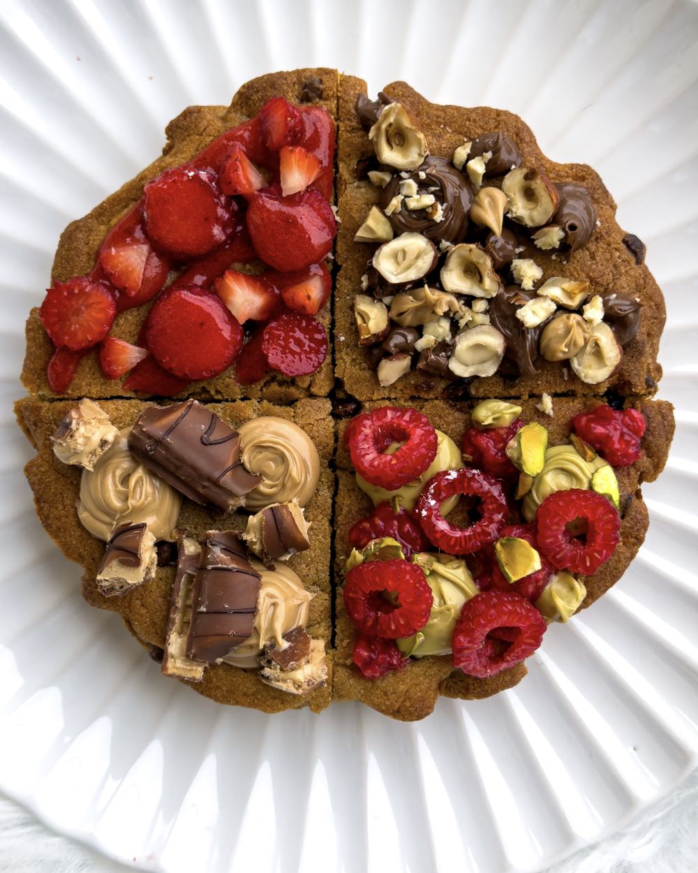 Cookie géant en quatre parts : fraises, noisettes et chocolat, crème praliné et barres chocolatées, framboises et pistache