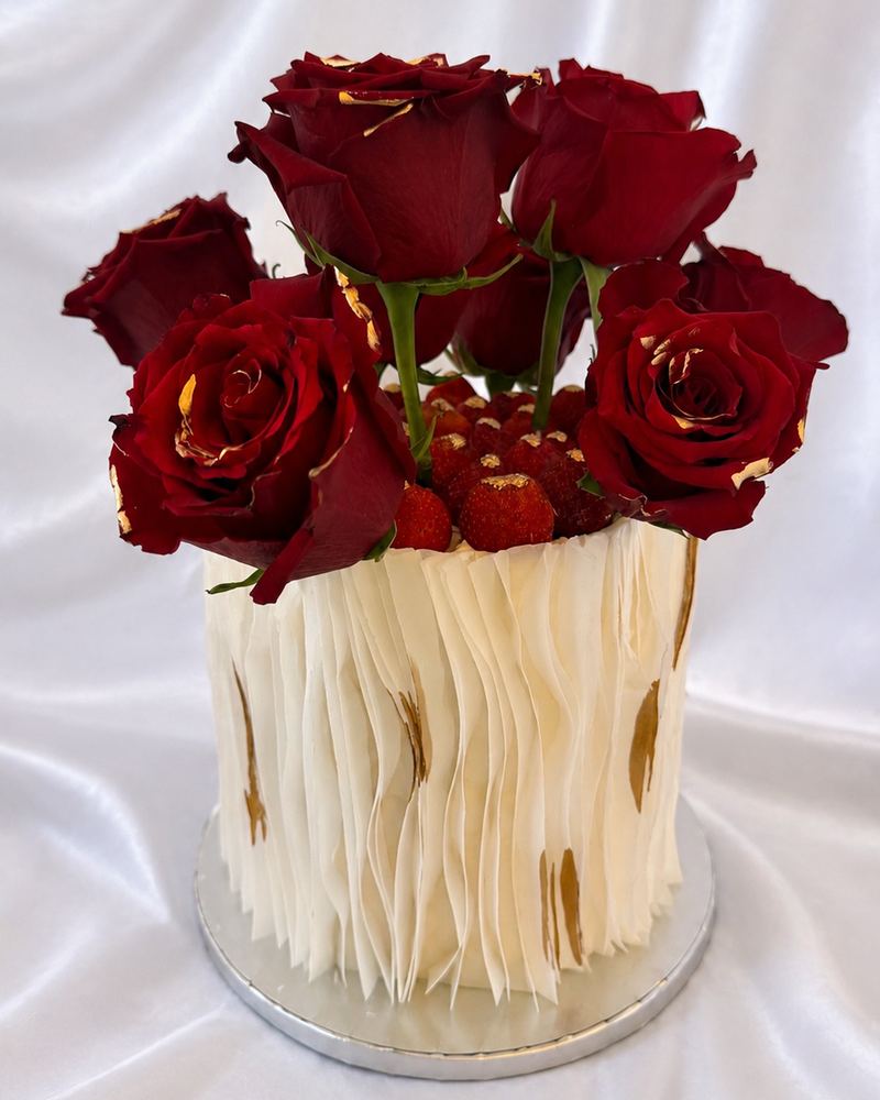 Layer cake blanc aux plis de crème, couronné de roses rouges et de fraises, touches de feuille d'or